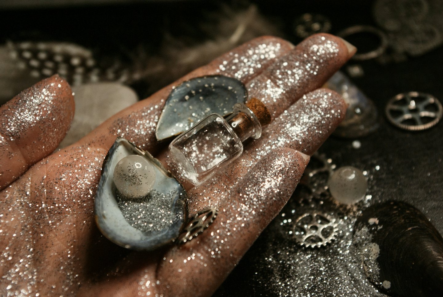 Mit Glitzer bedeckte Hand, die Muschelschalen und kleine Schmuckstücke hält.