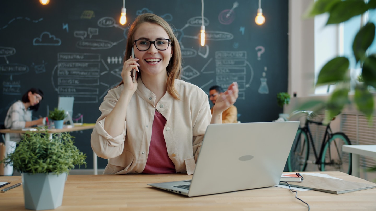 Eine Frau mit Brille telefoniert in einem modernen Büro.